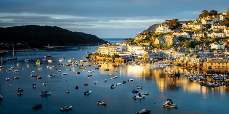 river full of boats and yachts at sunrise with golden light shining on a town on the right side bank on the river - salcombe devon