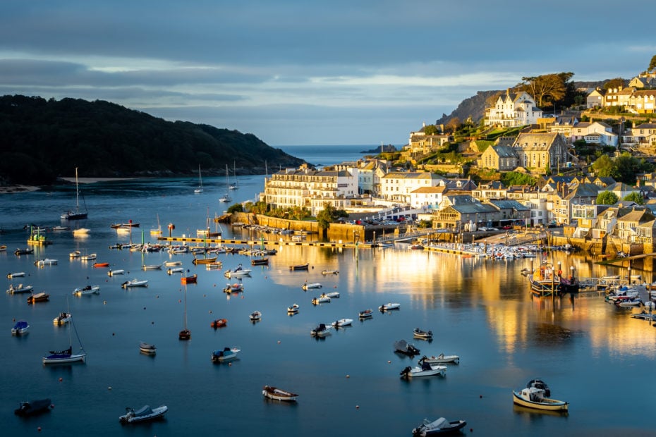 river full of boats and yachts at sunrise with golden light shining on a town on the right side bank on the river - salcombe devon