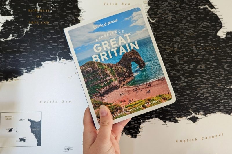 close up of a hand holding a book with durdle door on the cover and the title Lonely Planet Experience Great Britain. 