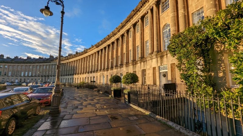 exterior of the royal crescent hotel with beige coloured stone town houses alongside a grey flagstone pavement near sunset with warm light on the buildings. Royal Crescent Hotel and Spa Bath Review.