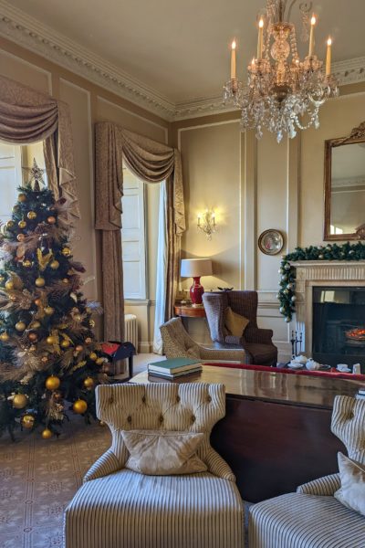 interior of a lounge with cream walls and some antrique cream arm chairs beneath a crystal chandelier. there is a fireplace behind and a decorated christmas tree to the left. Royal Crescent Hotel and Spa Bath Review. 