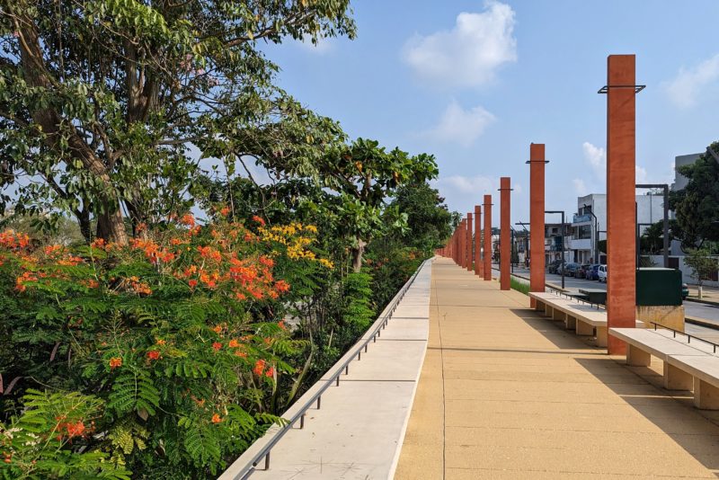 beige paved promenade with red rectangular pillars spaced along it on the right and thick tropical greenery on the left - best things to do in villahermosa