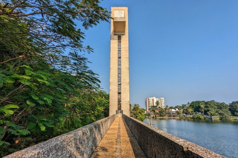 stone pathway leading towards a tall rectangular shaped tower made from beige coloured stone with a blue lake on the right on a very sunny day in villahermosa mexico