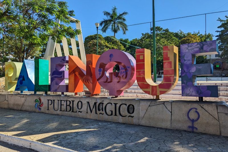 sign with letters in different colours of the rainbow spelling out the word Palenque with blue sky and palm trees behind on a very sunny day