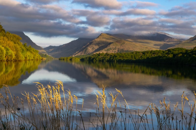 view of a very calm flat lake reflecting the sky on a sunny morning with mountains in the background 