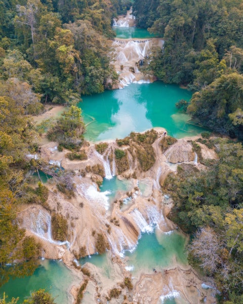 aerial shot of a jungle with several large bright green pools with several small waterfalls linking each pool