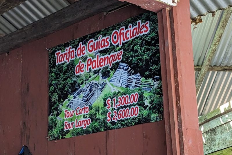 a red wall with a large poster on it showing a photo of palenque ruins from above with the following words printed in red over the top: tarifa de guias oficiales de palenque tour corto $1300 tour largo $2600