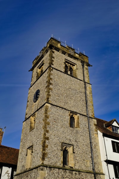 Looking up at a grey stone rectangular shaped clock tower against a blue sky