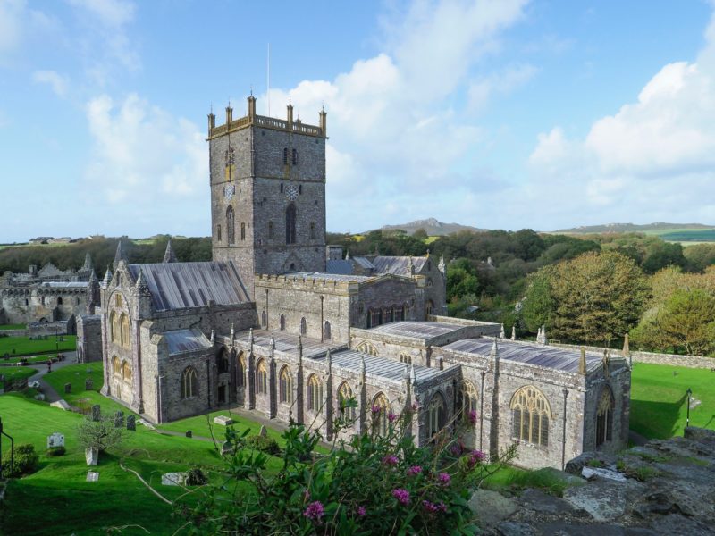St Davids Cathedral - a grey stone cathedral with a square tower surrounded by green trees woodlands and countryside