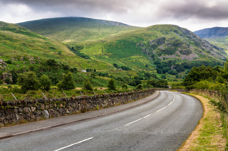 Curved road in countryside surrounded with mountains on a cloudy summer day - best wales road trips