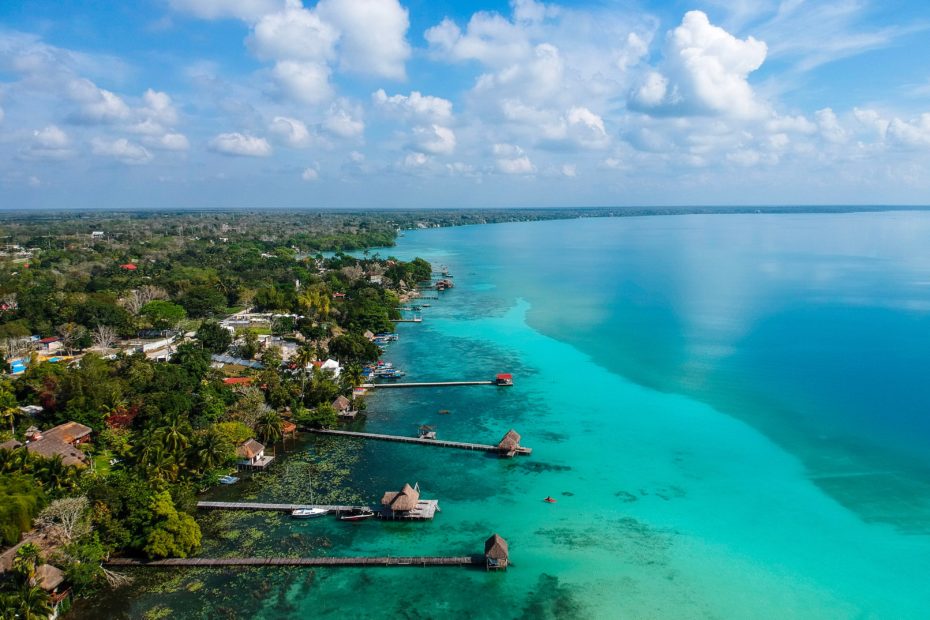 aerial photo of a huge lagoon with striking turquoise water and the shore covered in green tropical forest with several long wooden jetties reaching out into the lake