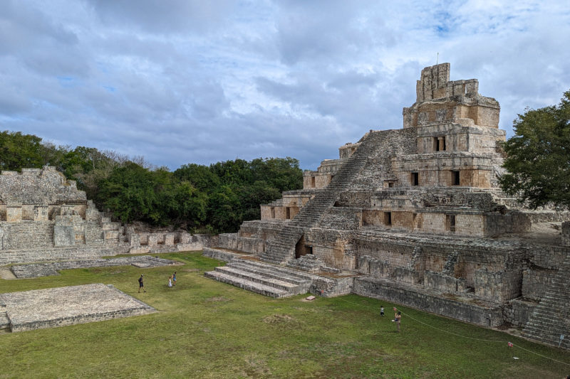 large square grass field in front of a large grey stone mayan pyramid with 6 levels at Edzna Archeological Site in Mexico