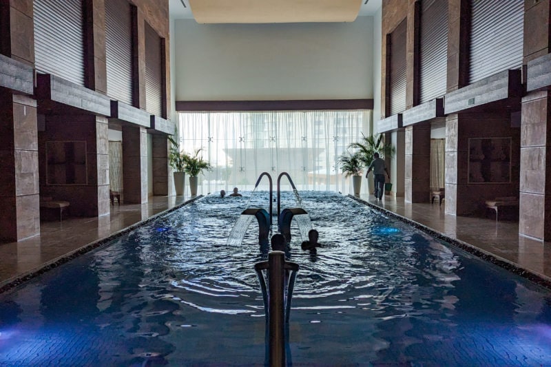 indoor pool in a dimly lit room with a large window at the far end and wooden panelled walls on either side