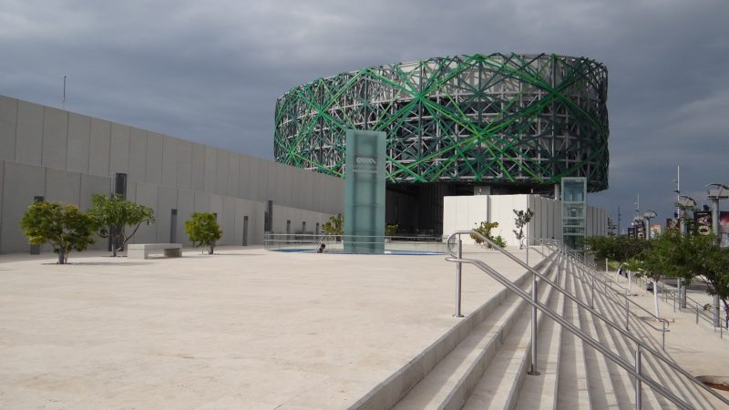 white stone steps and white stone patio area outside the Mayan Museum in Merida with a large circular building of green metal and glass