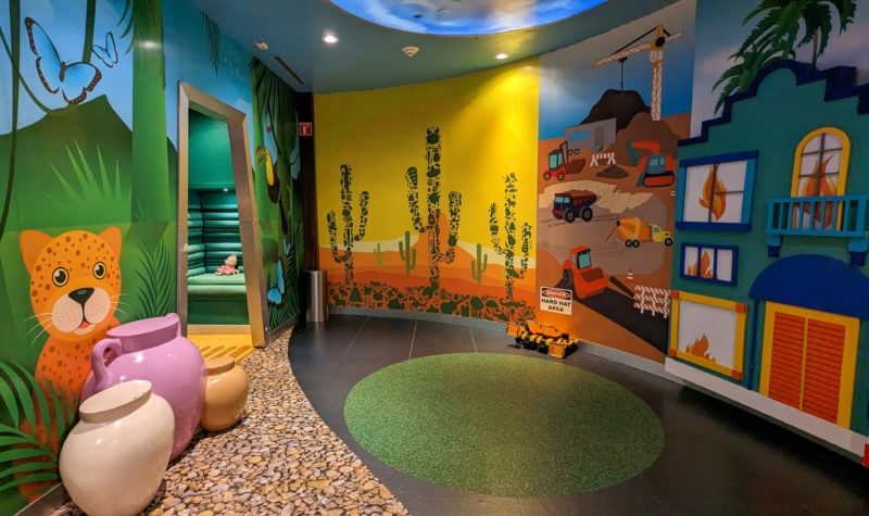 interior of a childrens game room with the walls painted in bright coloured murals with a cartoon tiger and jungle scene on the left and a cartoon of a burning building on the right. 