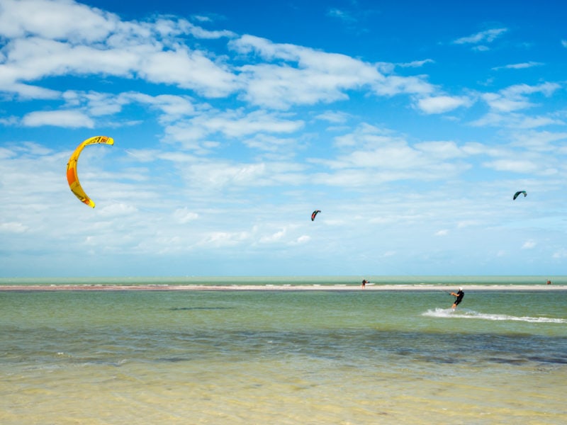 man kitesurfing with a yellow kite in the sea on a sunny windy day with blue sky behind him