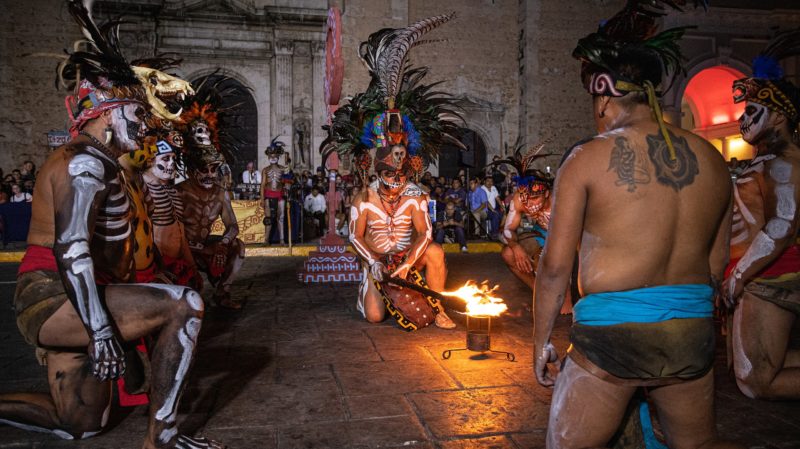 group of Mexican men in traditional mayan costume with body paint and feather headresses around a small fire getting ready for a pok ta pok game in Merida