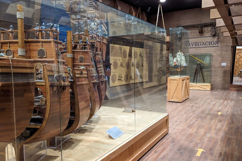 interior of Museo El Palacio in Campeche with a wooden model of a ship in a glass case and several exhibits out of focus behind that one.