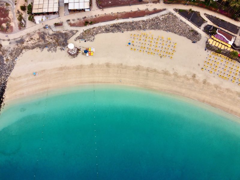 drone shot looking staight down at a white sandy beach with rows of umbrellas next to a turquoise sea 