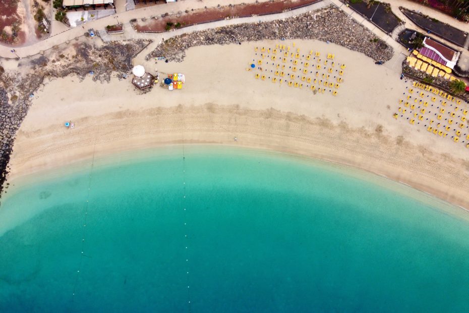 drone shot looking staight down at a white sandy beach with rows of umbrellas next to a turquoise sea