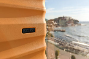 close up of the side of a mustard yellow hard shell suitcase with a black handle on a hotel balcony next to a glass panel with a view of the ocean and marina out of focus behind - Antler Clifton Luggage Set Review