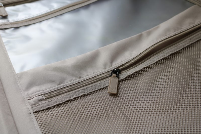 close up of two interior pockets inside a suitcase made from grey fabric with grey zips. one pocket is mesh the other is clear plastic. 