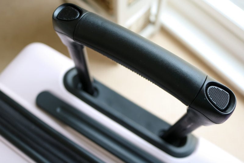 close up of a black handle extended from the top of a pale pink suitcase with black trim 