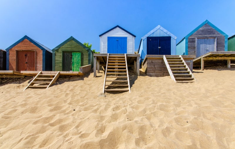 row of colourful beach huts on a golden sandy beach with blue sky above