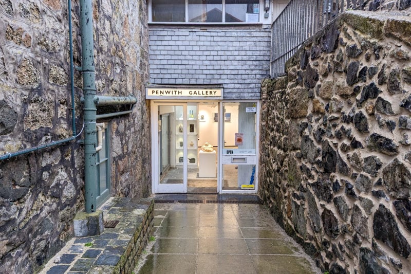 narrow alley between two brown stone building walls with a large glass door at the end of the alley and a sign raeding 'penwith gallery'