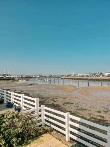 white picket fence next to a sandy beach with a small marina behind and blue sky overhead
