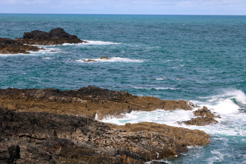 blue sea with small brown rocky islands in and white capped waves hitting the rocks