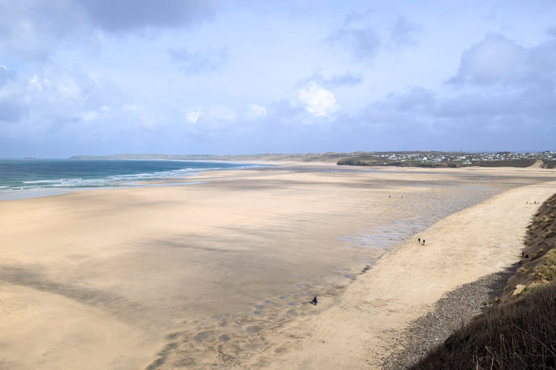large white sandy beach at low tide with the sea in the distance and a hazy blue sky overhead with some grassy dunes just visible in the far distance - taken from the south west coast path along st ives bay in cornwall england