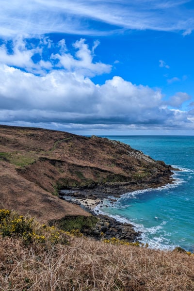 sloping grassy cliffs next to a bright turquoise sea on a very sunny day with blue sky and white clouds overhead - hiking the coast path from St Ives to Zennor