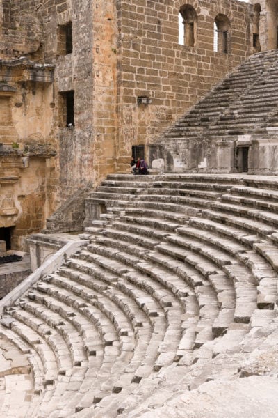 section of an ancient theatre in turkey with curved rows of grey stone steps alongside a beige stone wall