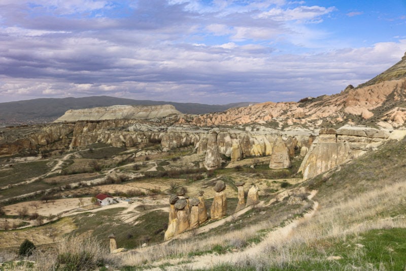 dry valley filled with tall conical rock stacks. The floor and rocks in the valley are yellow sandy coloured stone with small patches of grass growing here and there and blue cloudy sky overhead.