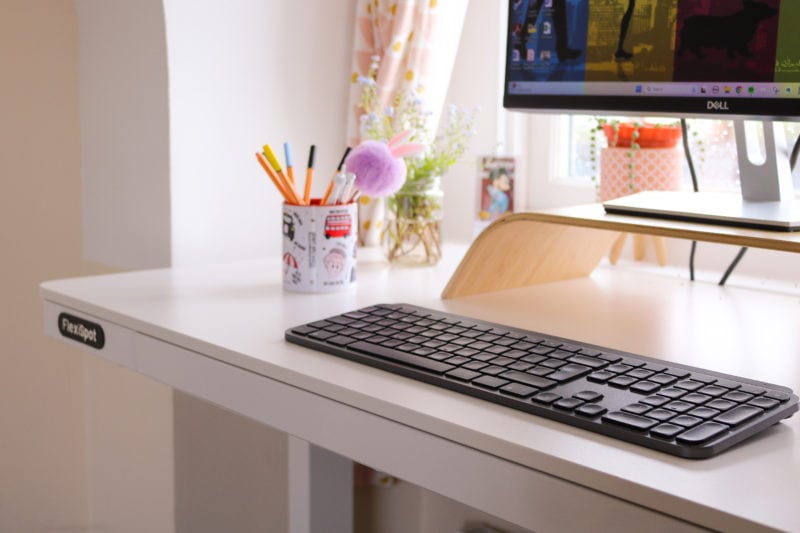 corner of a white wooden desk top with a black keyboard, a mug of pens and the lower half of a monitor visible. FlexiSpot Comhar EW8 review. 