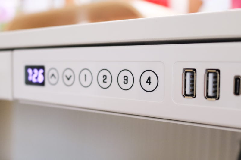 close up of the front edge of a desk with a row of buttons showign an up arrow, a down arrow, followed by numbers 1 to 4. the buttons are in a line next to a small led display with the number 72.6 displayed. there are also two usb ports on the other side of the buttons.