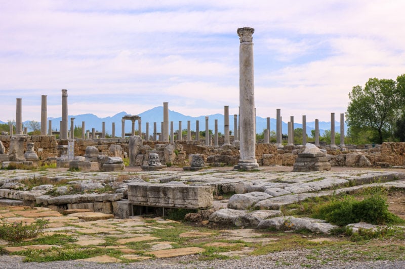 landscape with distant blue mountains in the background and a large number of stone pillars, some complete and some in ruins, on the ancient stone streets of Perge near Antalya