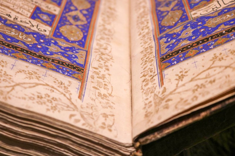 close up of the spine and open lower corner of a very old book with gold floral designs around the edges of the pages and the corner of a blue and gold design visible at the centre of the page. An ancient quran in the Mevlana Museum in Konya Turkey