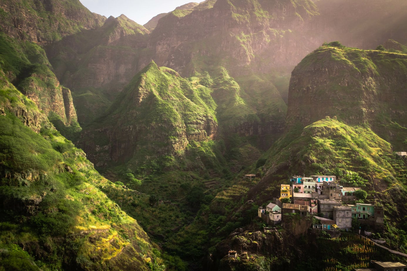 a wall of green mountains with a small village of colourful houses nestled amongst them in Cape Verde