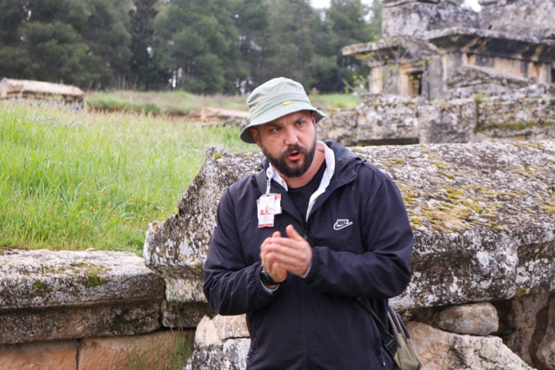 a turkish man with a beard wearing a khaki bucket hat and a black raincoat giving a tour in front of ancient ruins in Hieropolis.  Jet2 Treasures of Turkey review.