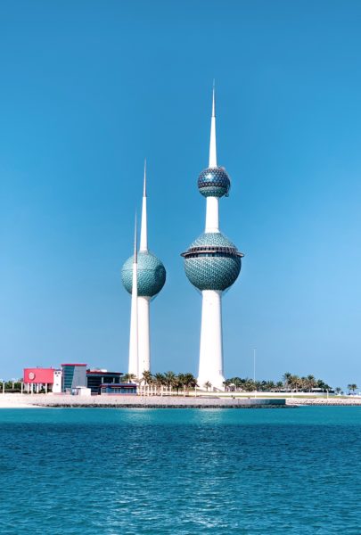 two white towers with turquoise domes halfway up next to the sea in kuwait