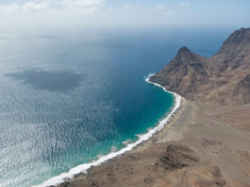 aerial view of the edge of an island with dry rocky cliffs surrounded by blue sea