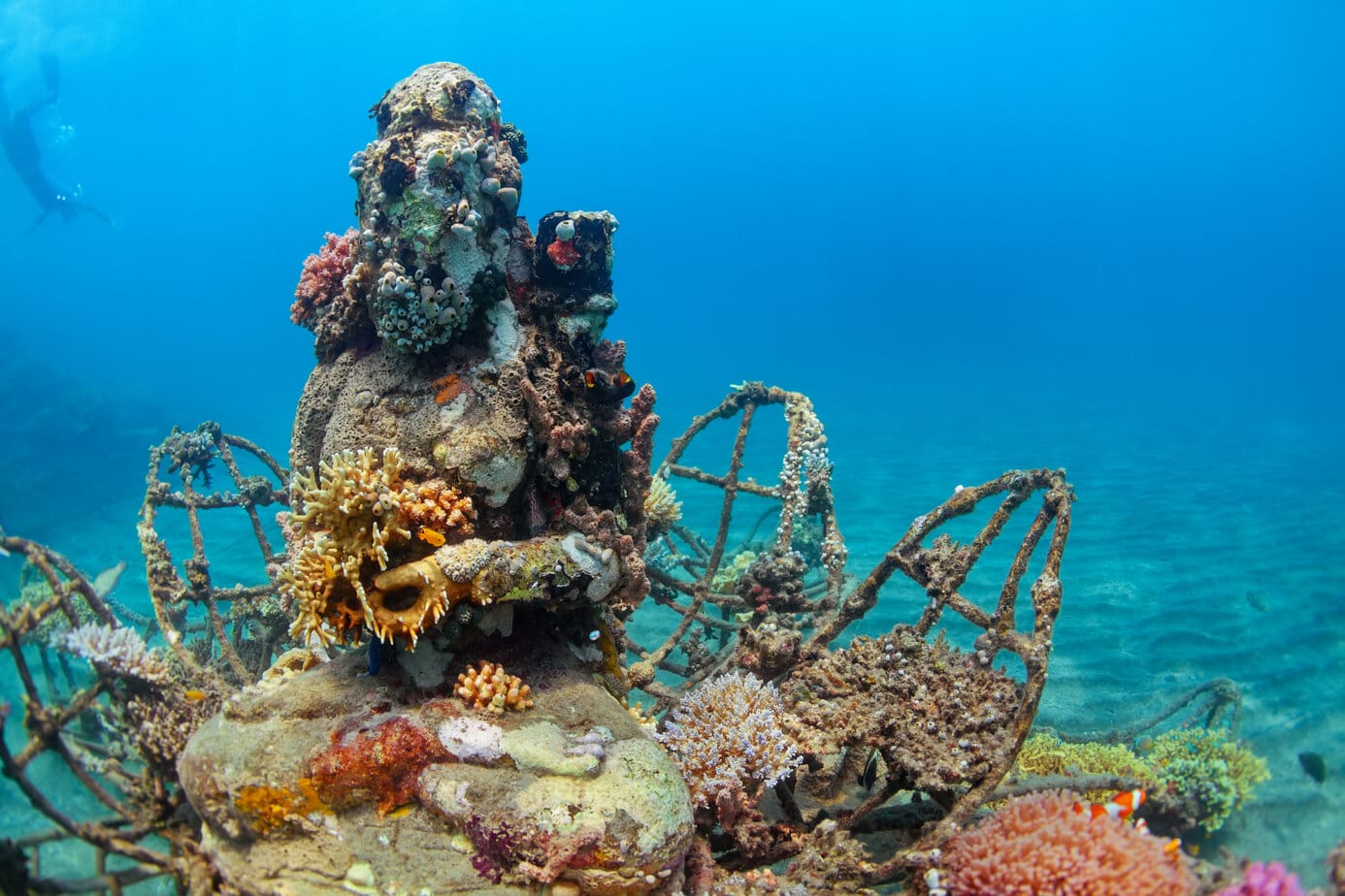 Buddha statue on sea sand bottom on background of snorkeler swimming deep down into water to observe tropical reef. Snorkel and scuba diving sites in Bali, Indonesia.