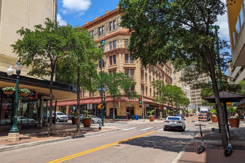 Street in San Antonio Texas with a large six storey building of pale orange bricks visible between the trees ion either side of the street