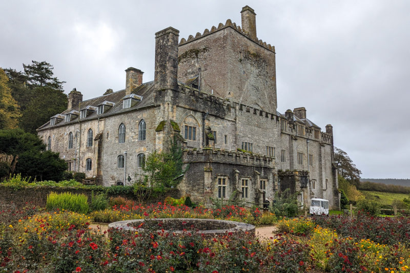 large English country manor house built from grey stone with a smal garden in front and grey sky behind