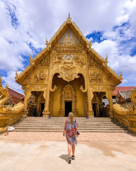 emily wearing a long orange shawl with flower pattern walking towards a large temple completely painted bright gold in Nan Thiland. 