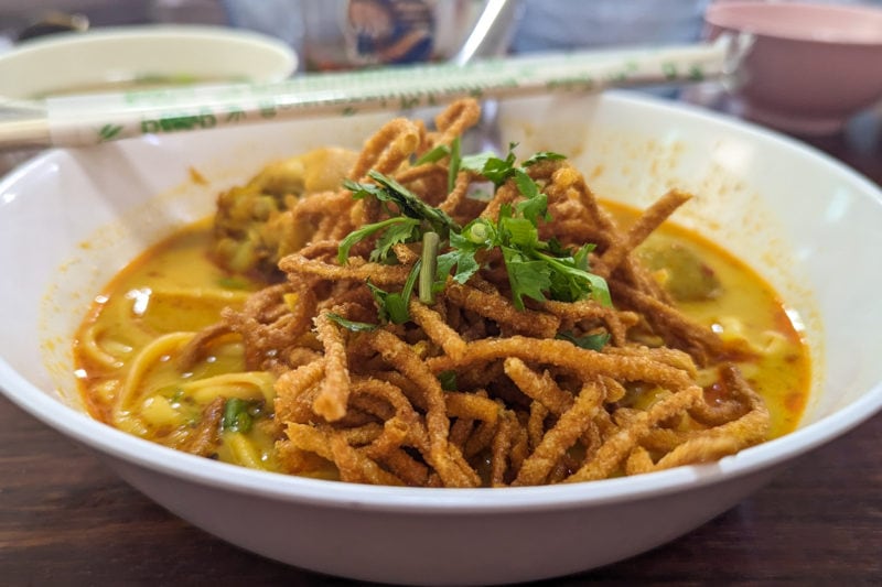 white china bowl filled with a yellow curry broth and cripsy fried noodles