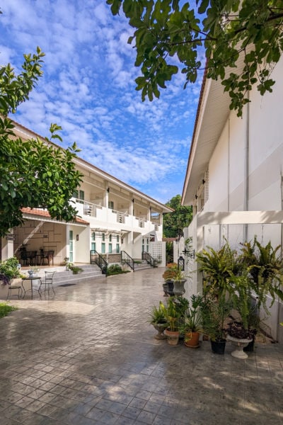 stone tiled courtyard between two white two-storey buildings of a small hotel. there are many potted plants in the courtyard. 