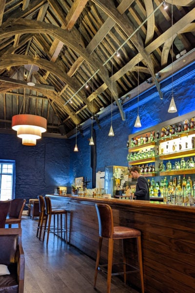 Inside the bar at Plymouth Gin Distillery with a young male bartender behind the long wooden bar and a high vaulted cieling with wooden beams